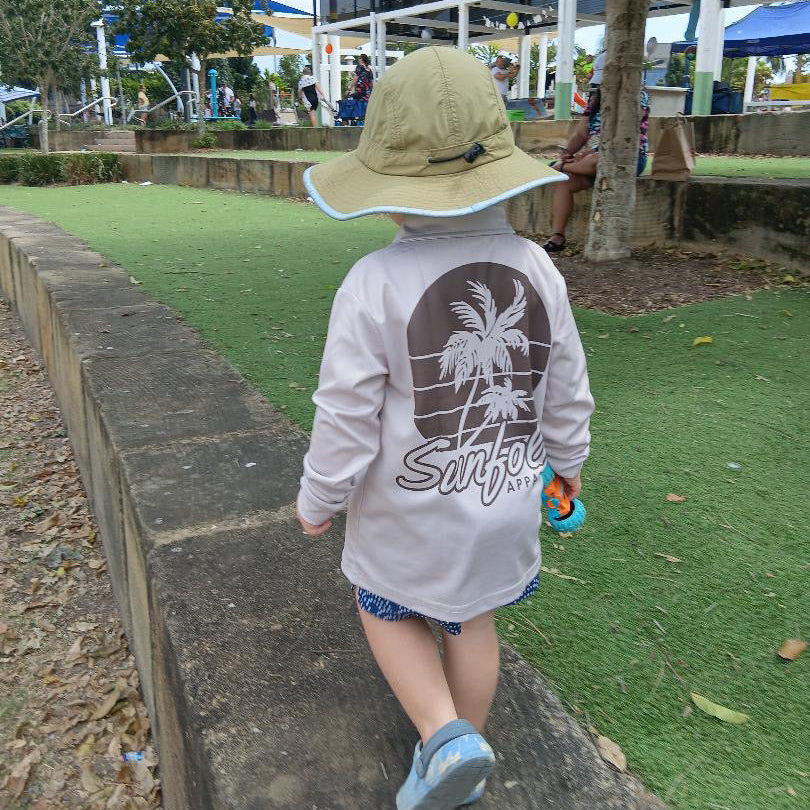 Child wearing a sun hat and Sunfolk Apparel shirt walking on a path in a park.