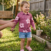 Child in a pink floral shirt standing in a garden with a person holding their hand.