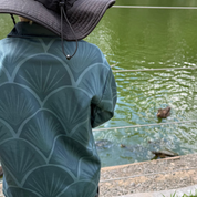 Child wearing a black hat and green patterned shirt standing by a pond with ducks.