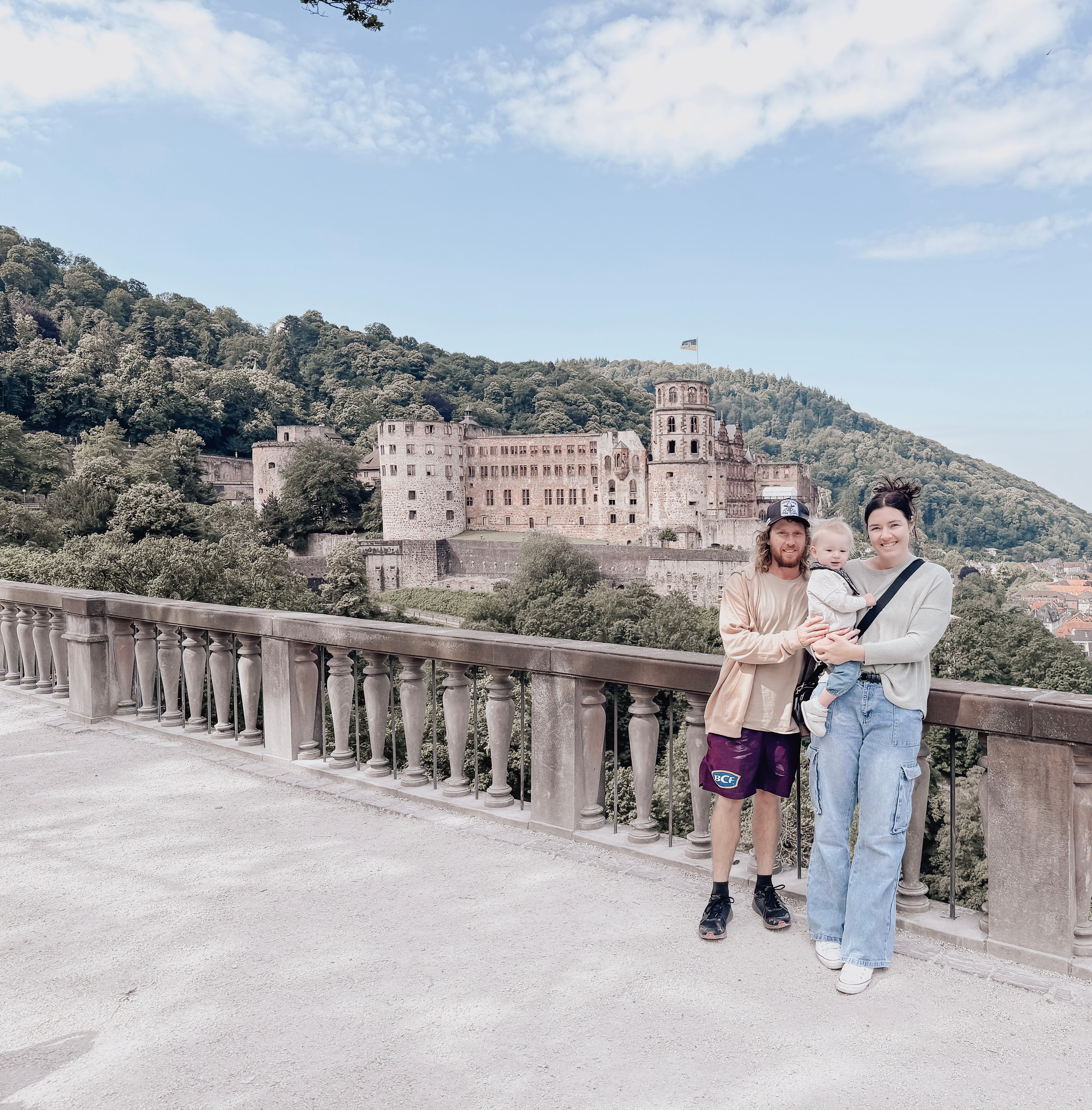Two adults and a child standing on a bridge with a castle in the background
