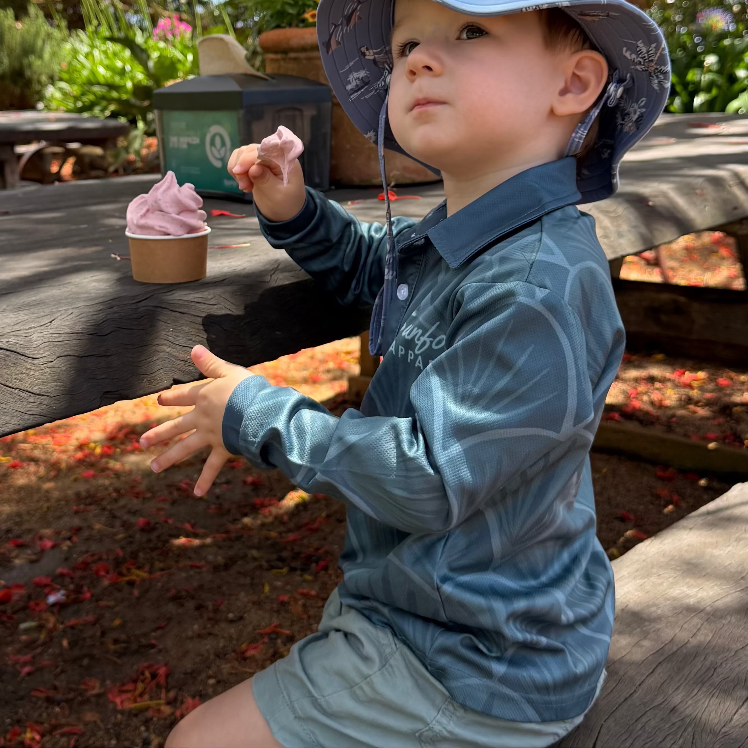 Child sitting at a picnic table outdoors with an ice cream cone