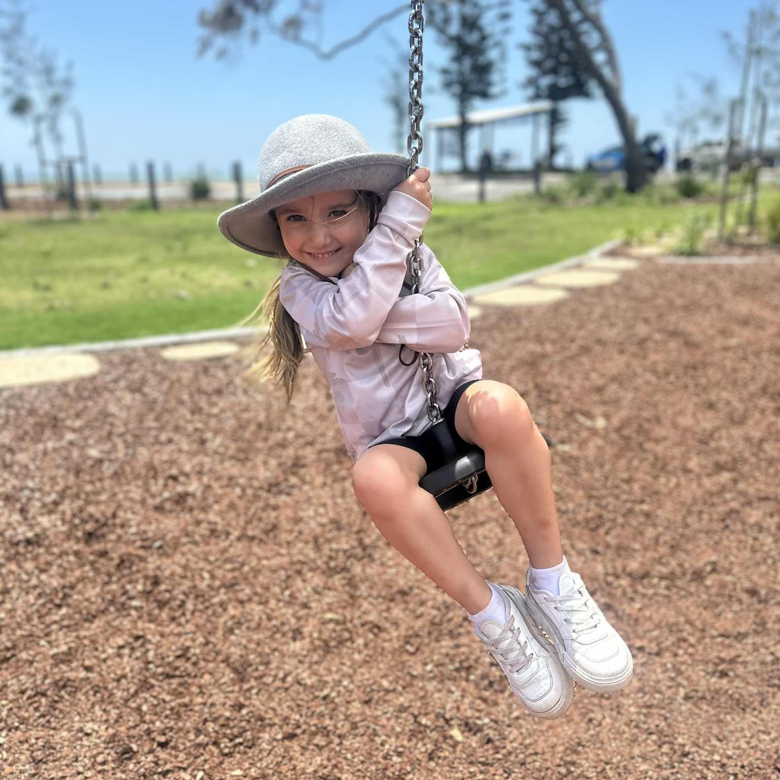 Child swinging on a playground swing set with a clear blue sky in the background