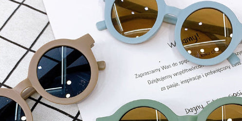 Four pairs of colorful sunglasses on a white paper with text, placed on a grid-patterned surface.
