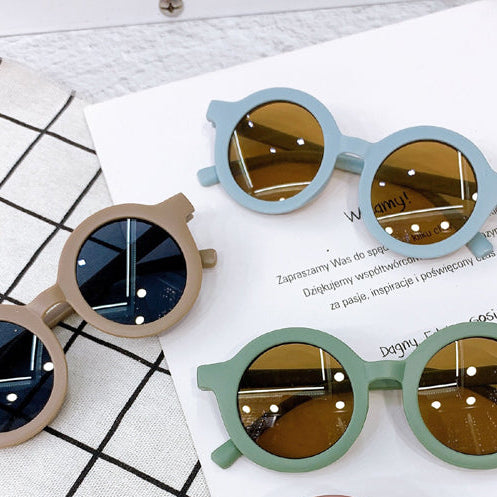 Four pairs of colorful sunglasses on a white paper with text, placed on a grid-patterned surface.