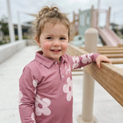 Child wearing a pink shirt with white flower patterns at a playground.