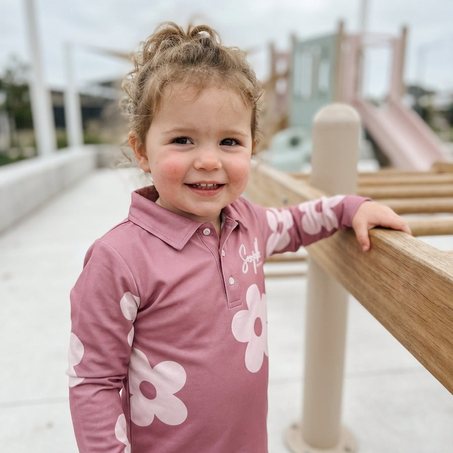 Child wearing a pink shirt with white flower patterns at a playground.